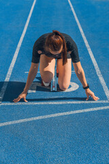 Obraz na płótnie Canvas Vertical shot of female athlete taking position on her marks before run, sprinter preparing at starting line, sportswoman ready for race, fitness training, speed, competition and athletic performance