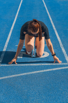 Vertical shot of female athlete taking position on her marks before run, sprinter preparing at starting line, sportswoman ready for race, fitness training, speed, competition and athletic performance