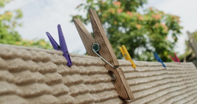 A woman uses her hand to fasten a large clothespin onto a blanket that is airing out on a clothesline outdoors in summer.