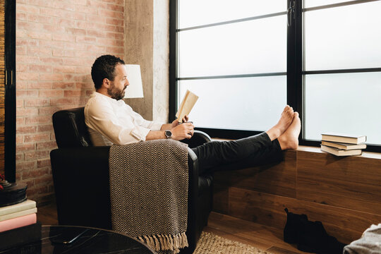 Person relaxing in armchair reading book at home