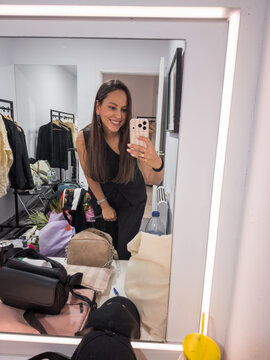 Smiling woman taking a selfie in front of a dressing room mirror.