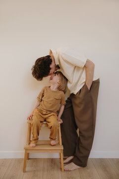 Loving father kisses his little son sitting on a wooden step stool