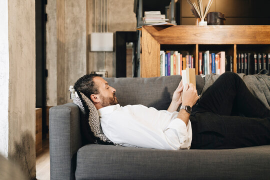 Person relaxing on couch reading book at home