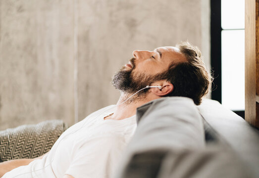Person listening to music in earphones relaxing on sofa