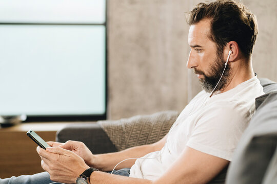 Person relaxing on sofa using smartphone and earbuds