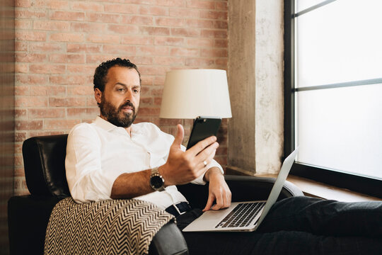 An elegant man works remotely while sitting in an armchair at home