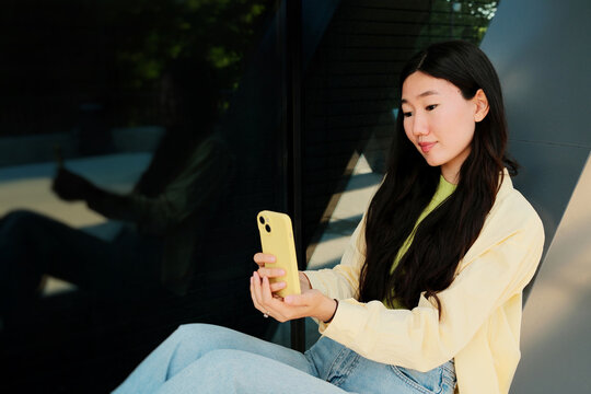Young happy asian woman listening during a video call in the street
