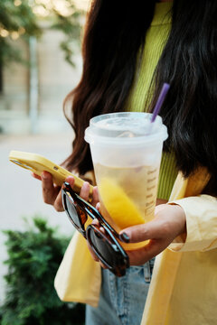 Close up crop of anonymous woman holding mobile phone and a cold drink