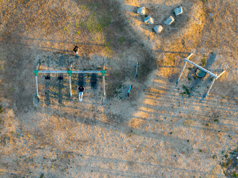 Aerial view of a person on a swing in a playground with dry grass and long shadows in Hook, England, United Kingdom.