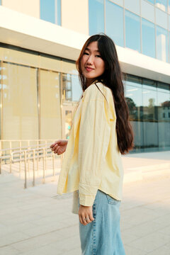 Young happy stylish asian woman standing in the city centre street