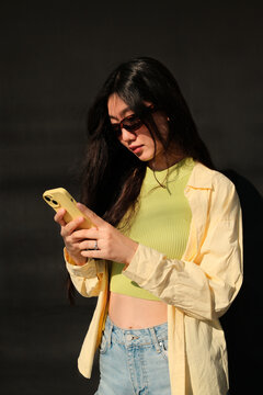 Young asian woman in sunglasses typing a message on mobile phone