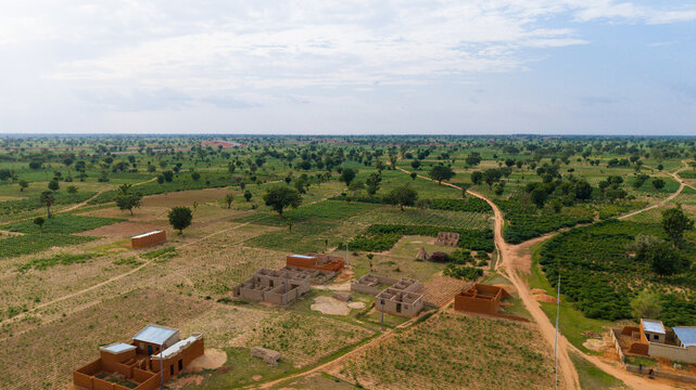Aerial view of rural landscape with scattered mud-brick houses, dirt paths, and agricultural fields under a cloudy sky in Dambatta, Kano, Nigeria.