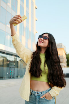 Young happy asian woman with smartphone making selfie in city street