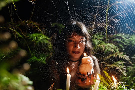 Woman with Owl Candle in Fern Forest at Night seen through spiderweb