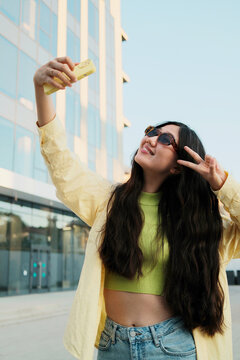 Happy asian female tourist with smartphone making selfie in the street
