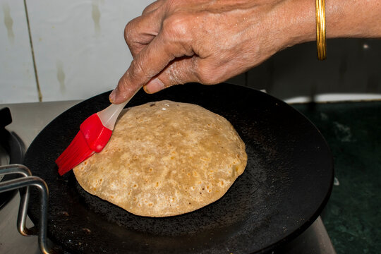 lightly brushing ghee or butter onto a paratha while cooking it on a hot tawa, mindful approach to using a small amount of cooking fat in everyday cooking