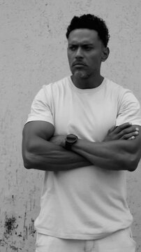 African American man standing with arms crossed against textured wall in black and white