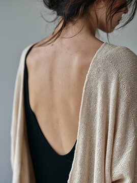 Close-up of the back of a woman's upper body. she is wearing a black tank top and a beige cardigan. the cardigan is open, revealing her bare back.