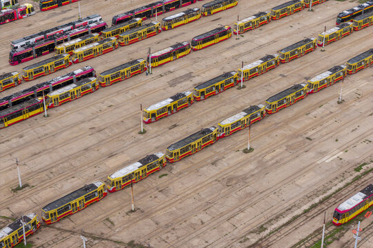Aerial view of a large tram depot in Poland featuring rows of modern and vintage yellow and red trams parked on parallel tracks.