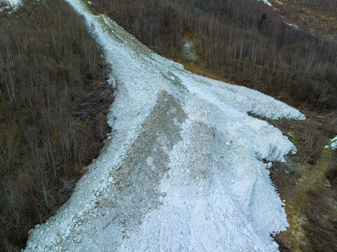 Aerial view of a large avalanche path cutting through a dense forest, showing debris and snow accumulation on the mountainside in Fjord, More og Romsdal, Norway.