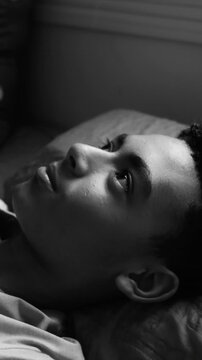 Pensive teenage boy lying in bed and looking up in deep thought in black and white