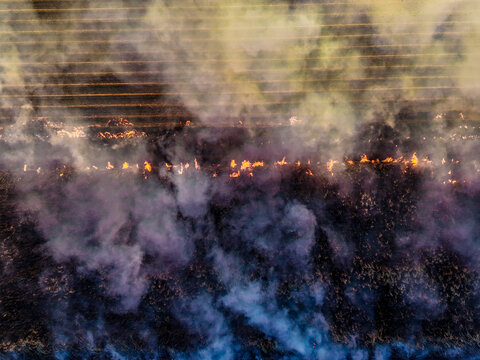 Aerial view of a controlled agricultural burn in a field with flames and thick smoke rising over the landscape in Home Hill, Queensland, Australia.