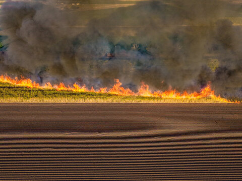 Aerial view of a controlled field fire burning across dry grass with thick smoke rising above a plowed field in Home Hill, Queensland, Australia.