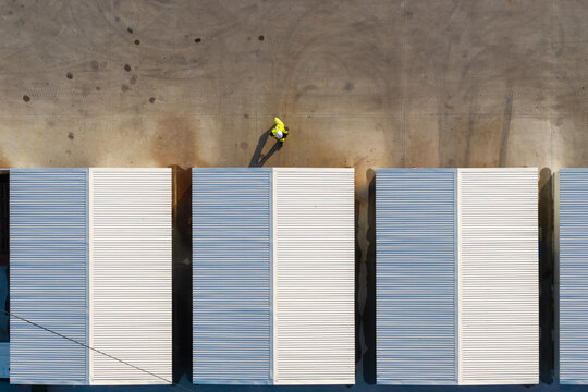 Aerial view of a worker in a high-visibility jacket walking past temporary storage containers at a construction site in Warszawa, Poland.