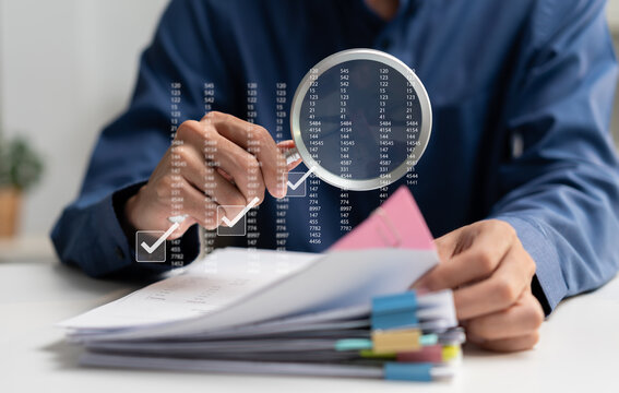 Businessman reviews financial documents with a magnifying glass, checking data and records for accuracy, compliance, audit, verification, risk management, and quality control.