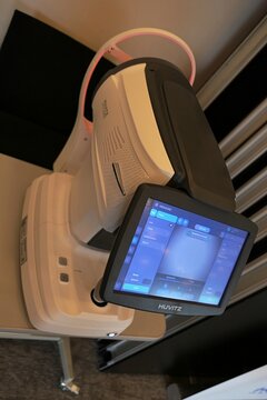 Examiner side of modern South Korean optical coherence tomograph Huvitz HOCT 1/1F, touchscreen with diagnostic menu opened. Displayed on medical expo. Joystick and control buttons also visible. 