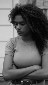 Sad and pensive Hispanic teenage girl standing outdoors with crossed arms in black and white
