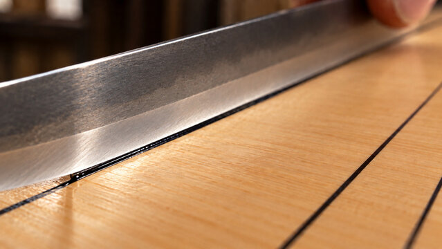 Close up of a steel blade applying black lacquer to a wooden game board