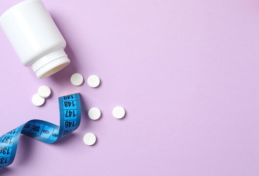 White jar of weight loss pills and measuring tape on color background