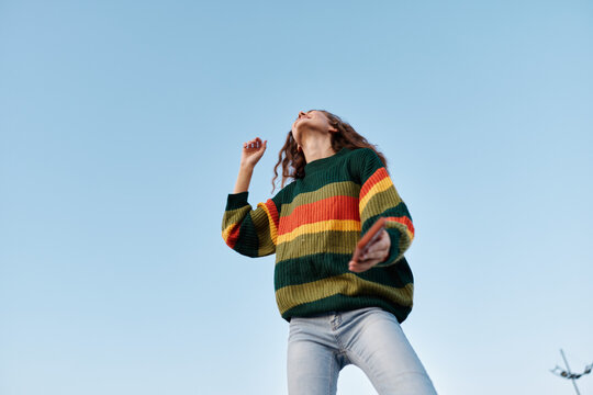 Colorful striped sweater worn by a person dancing in the open air, under a clear blue sky, conveying energy and playful fashion, suitable for lifestyle and travel themes.