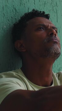 Close-up of African American man leaning against green wall looking upwards in pensive thought
