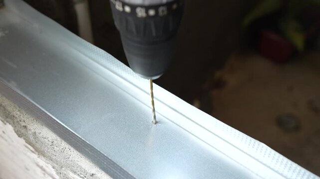 Close up of an electric drill making a hole in a metal drywall track