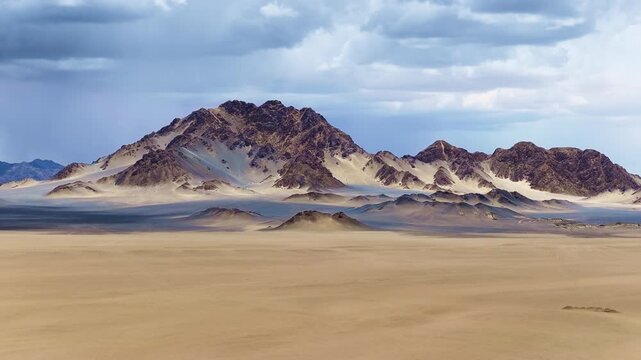 Dramatic landscape of rugged desert mountains rising from a vast arid plain beneath a dynamic cloudy sky in an extreme wilderness environment.