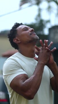Man looking upwards with clasped hands in prayerful devotion within peaceful urban surroundings