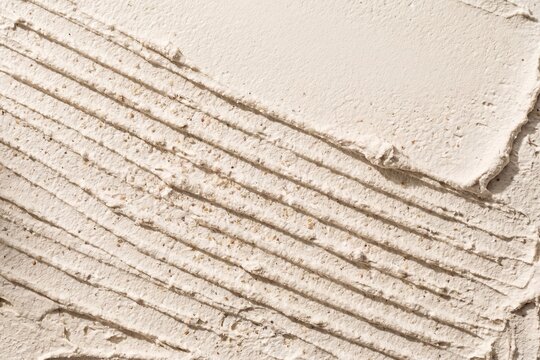 Combed Beige Plaster Texture Showing Trowel Marks and Ridges, A close-up of thick beige plaster or adhesive that has been applied and textured with a notched trowel, leaving distinct diagonal ridges
