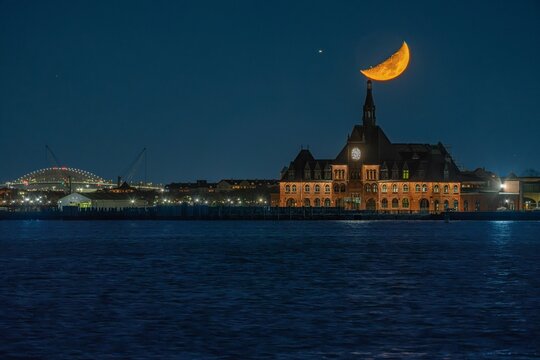 Aerial view of the Central Railroad of New Jersey Terminal illuminated at night with a crescent moon rising above the clock tower, Jersey City, New Jersey, United States.