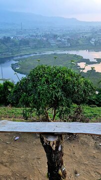 A bench with a view overlooking Danau Mas Harun Bastari in Rejang Lebong, Bengkulu, Indonesia. Features a green bush in the midground and a scenic lake during sunset.