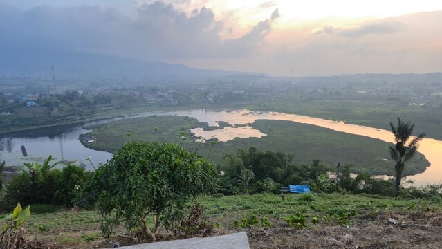 Danau Mas Harun Bastari in Rejang Lebong, Bengkulu, Indonesia. A tranquil high angle view of the lake at dusk with a warm golden sunset over the water, surrounded by tropical greenery and mist.