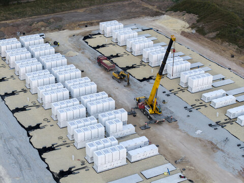 Aerial view of a BESS battery energy storage facility under construction with rows of white battery containers, a yellow mobile crane, and a dump truck in Trzebinia, Lesser Poland Voivode, Poland.
