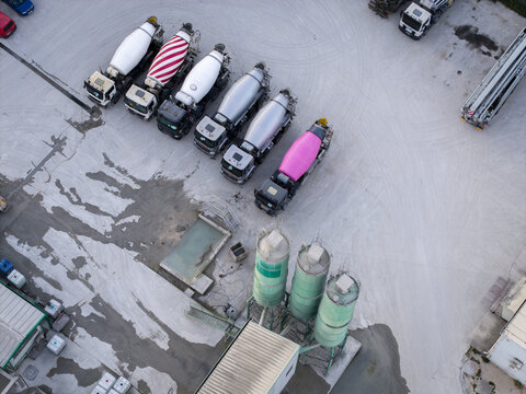 Aerial view of a concrete batching plant featuring a row of parked mixer trucks with colorful drums and industrial silos in a paved yard in Krakow, Lesser Poland Voivode, Poland.