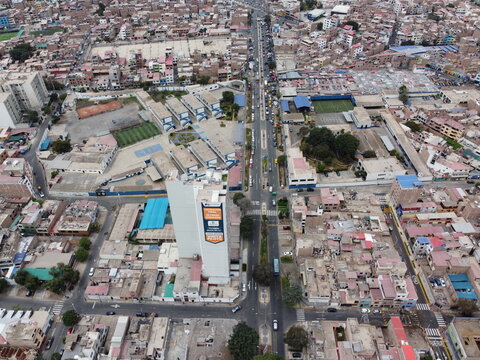 Aerial view of Avenida Jorge Chavez cutting through a dense urban neighborhood with residential buildings, schools, and sports fields in Santiago de Surco, Lima, Peru.