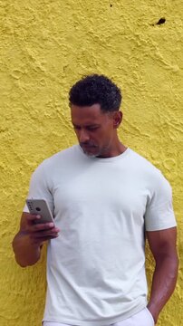 African American man holding smartphone against vibrant yellow wall in contemplative mood