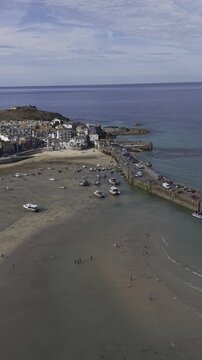 Cinematic vertical flight over the historic stone pier, lighthouse, and scenic harbor entrance in the beautiful coastal bay of St Ives.