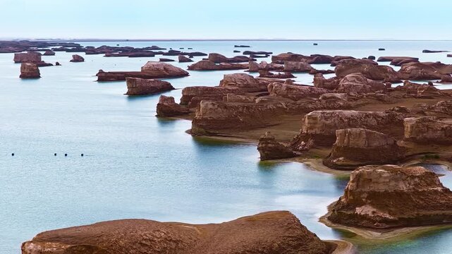 Aerial view of the unique water yardang landform with weathered sandstone rock formations rising above clear turquoise lake waters in Qinghai, China.