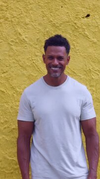 African American man smiling warmly standing against bright yellow textured wall outdoors