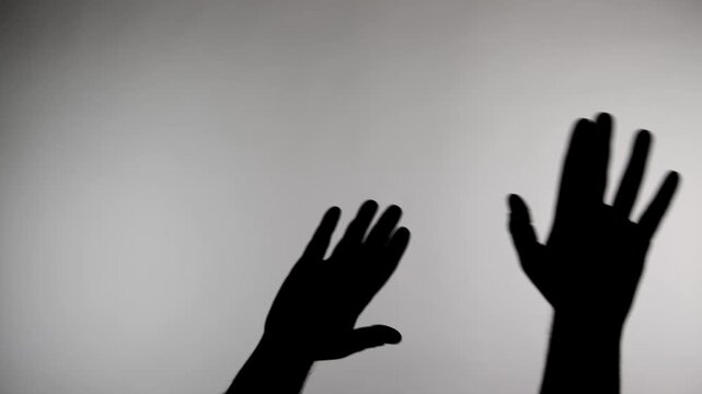 Hands reach up in different directions against a plain background creating a shadow effect